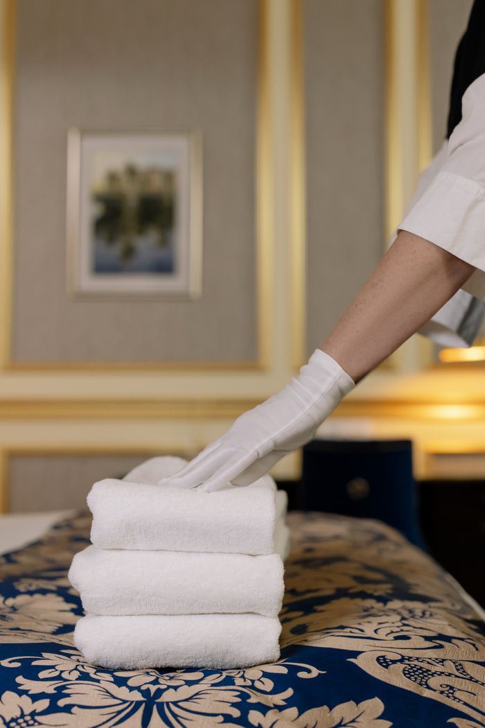 about-01 A hotel housekeeper in uniform arranges freshly laundered towels in a luxurious room.