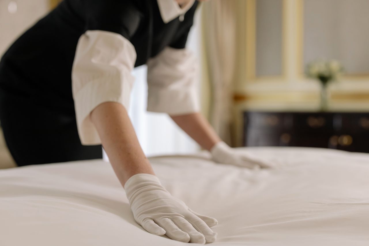 services-09 A housekeeper straightening the bed linens in a well-appointed hotel room.