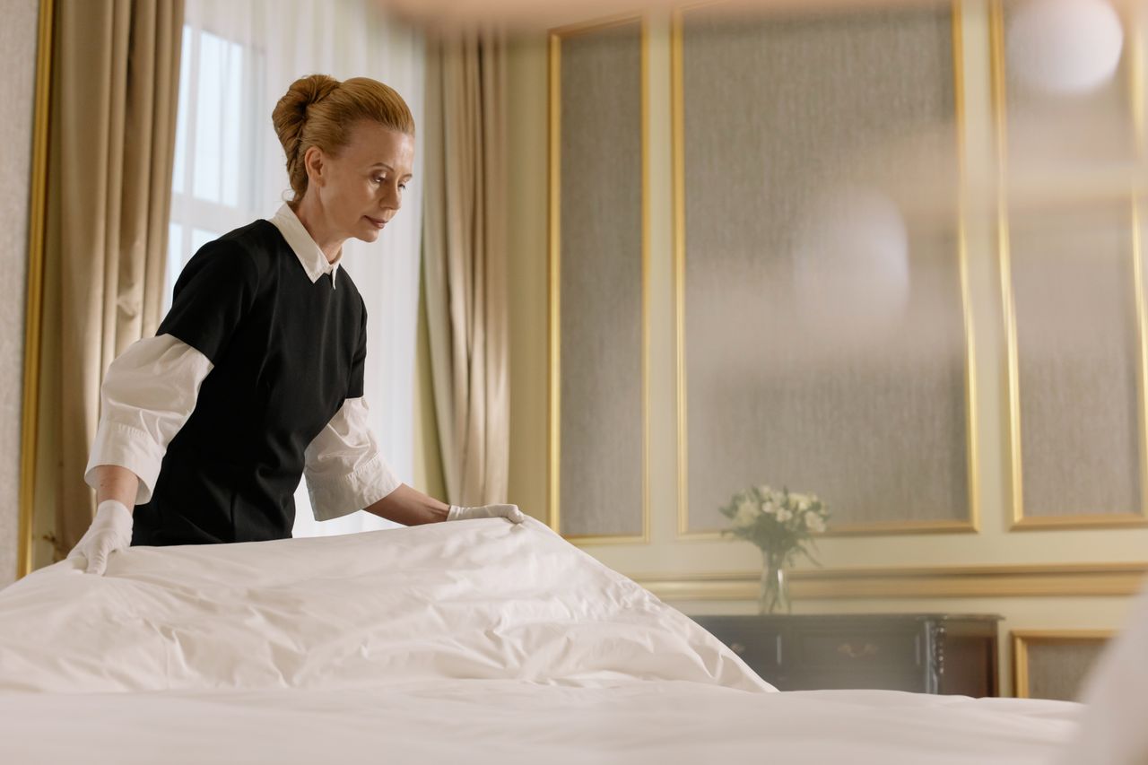 services-01 A professional housekeeper fixes a bed in a luxurious hotel room.